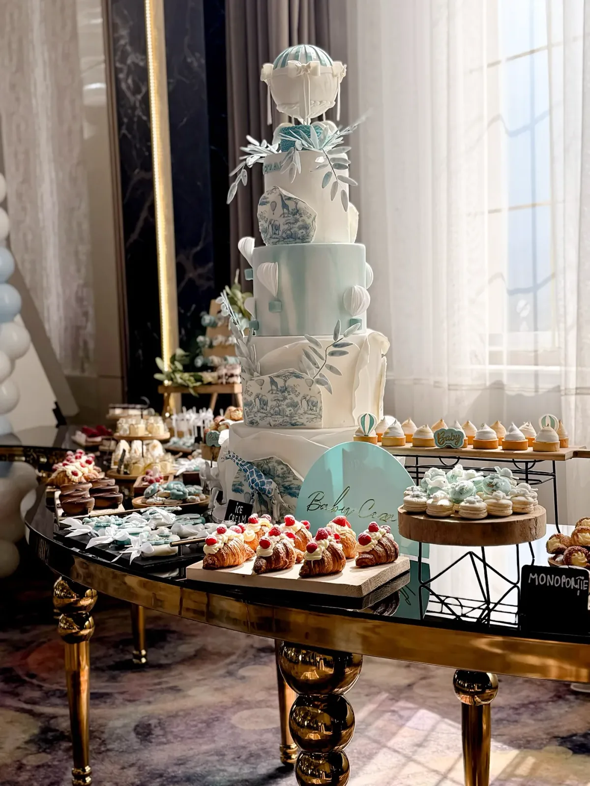 Tort etajat de botez în alb și bleu cu baloane cu aer cald din zahăr, pe masa de candy bar