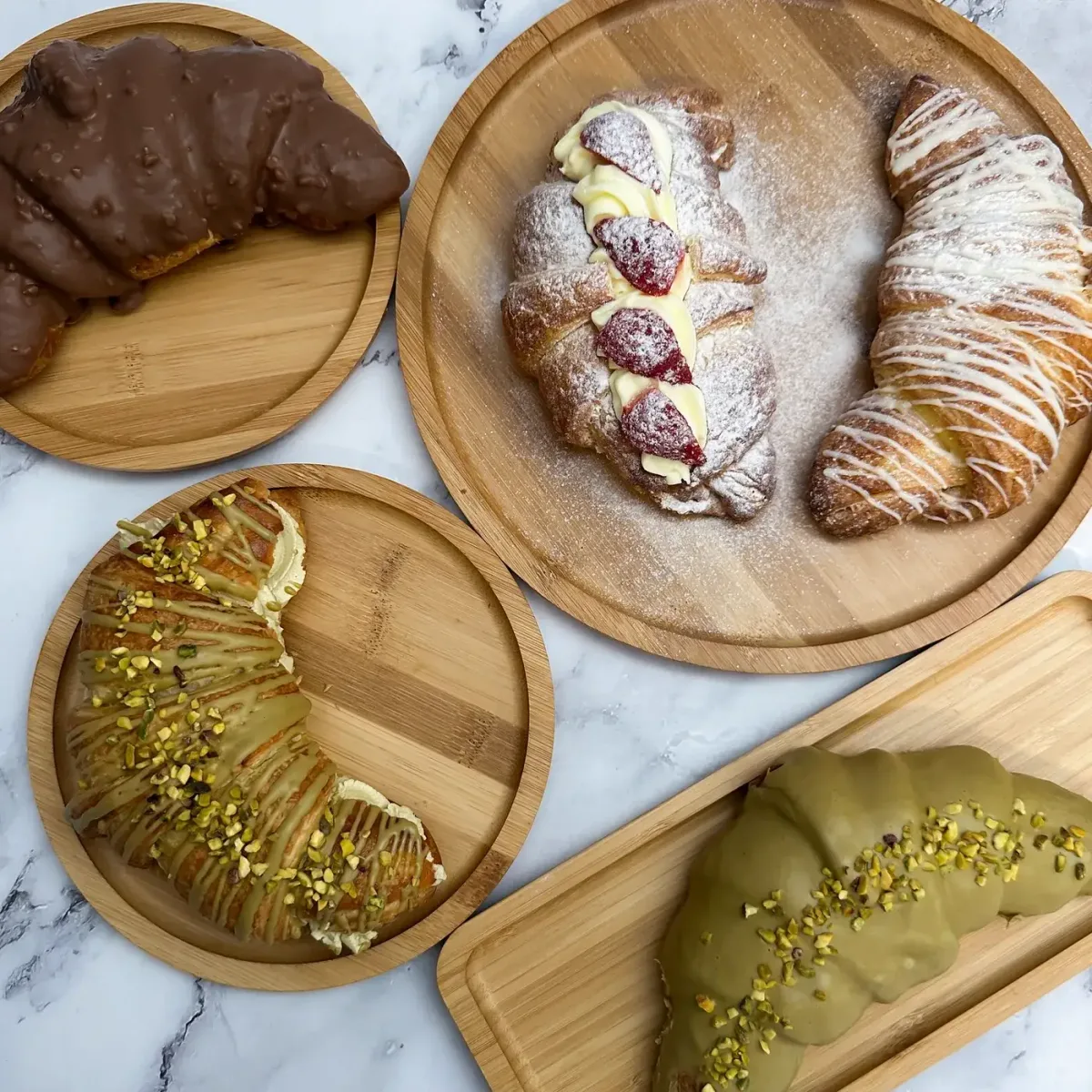 Croissante umplute cu cremă, căpșuni, ciocolată și fistic, servite pe platouri de bambus